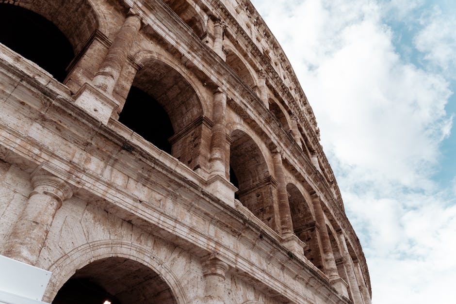 Detailed angle of the Colosseum's ancient stone arches under a partly cloudy sky in Rome, Italy.