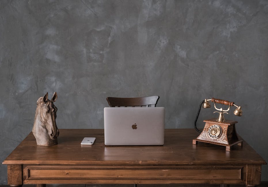 Wooden desk with opened laptop and telephone and vintage figurines on top against gray background